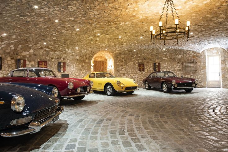 three classic cars are parked in a stone walled room with chandelier hanging from the ceiling