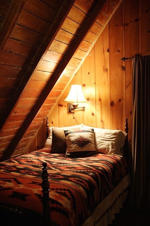 a bed in a room with wooden walls and a lamp on the side of it