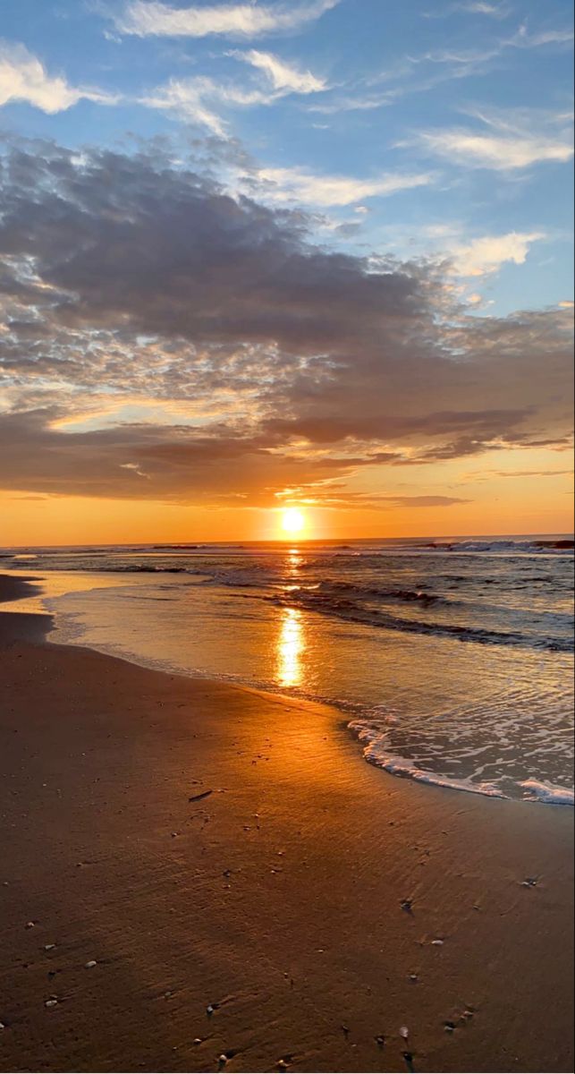 the sun is setting over the ocean with waves coming in