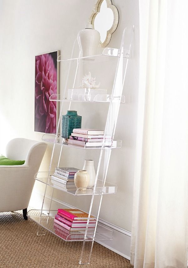 a white shelf with books on top of it next to a chair and table in front of a window