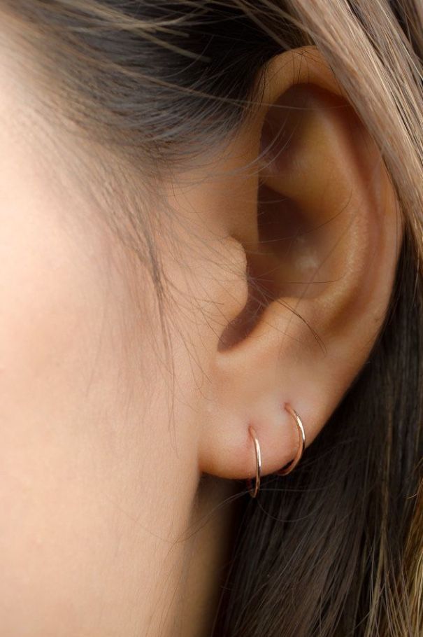 a close up view of a woman's ear with two thin gold hoops