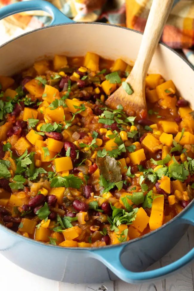 a pot filled with beans and vegetables on top of a wooden spoon next to a plate