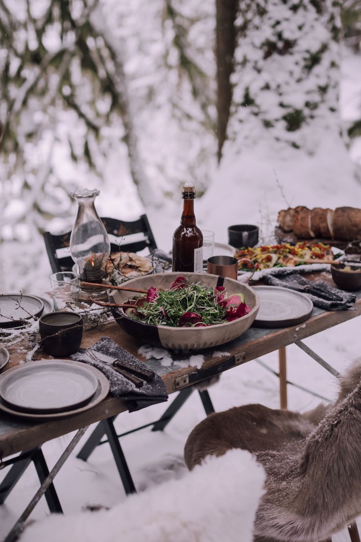 an outdoor table set with food and drinks in the snow