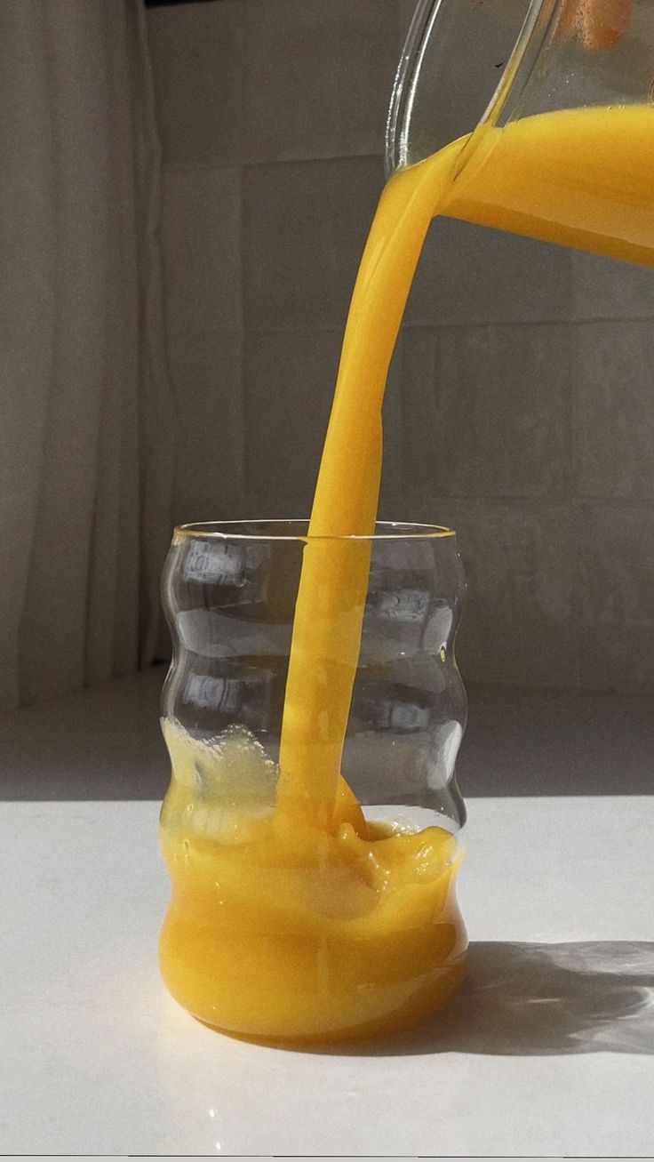 a glass filled with orange juice being poured into it's cup on top of a counter