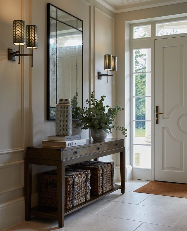 a hallway with a mirror, vase and two baskets on the floor next to it