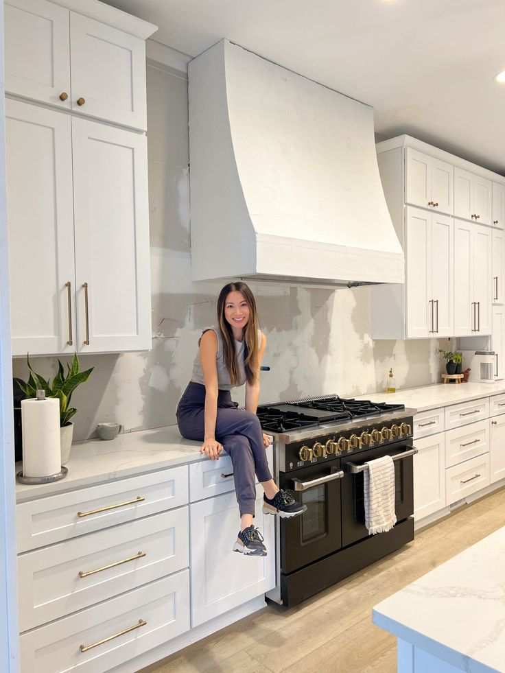 a woman sitting on top of a kitchen counter next to an oven and stovetop