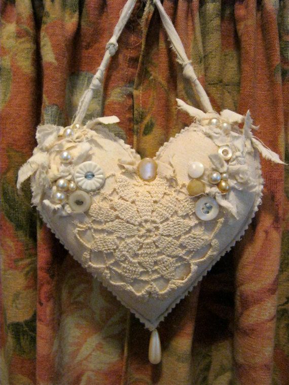 a white heart shaped bag hanging from the side of a curtain with buttons and pearls on it