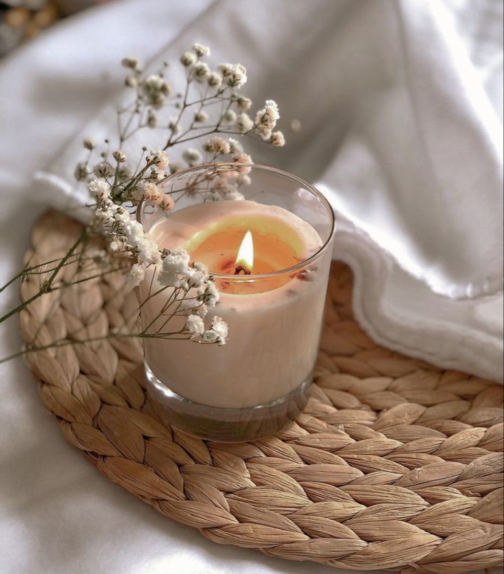 a small glass candle sitting on top of a wicker tray next to a white blanket