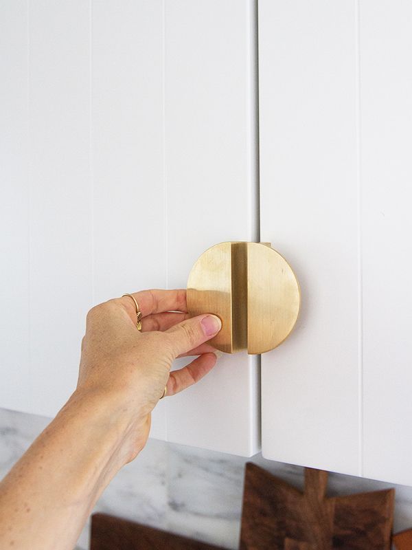 a person is holding the door knob to a cabinet with white cabinets in the background