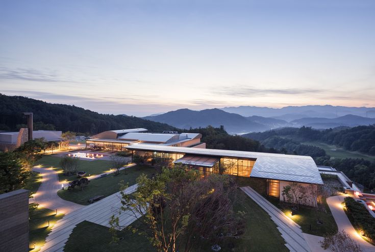 an aerial view of a building surrounded by trees and mountains at night with lights on