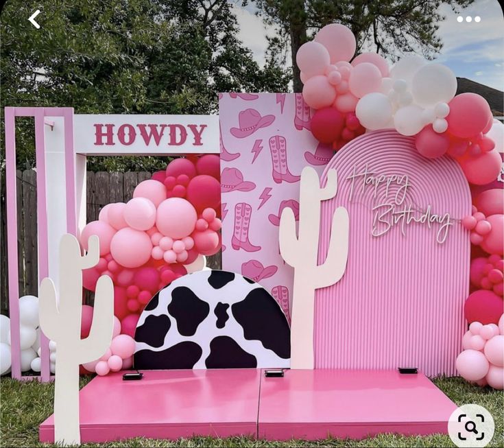 a pink and black cow themed birthday party with balloons on the wall, cactus decorations