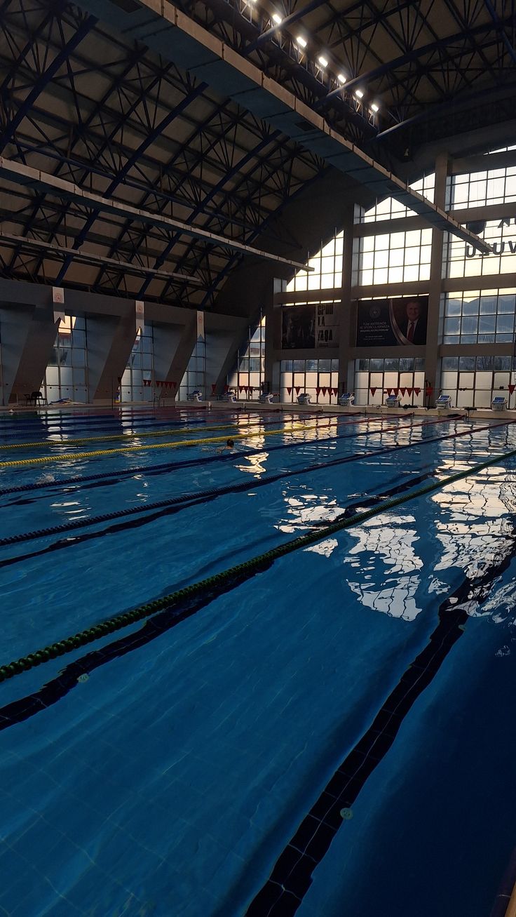 an indoor swimming pool with blue water and lights on the ceiling, surrounded by large windows