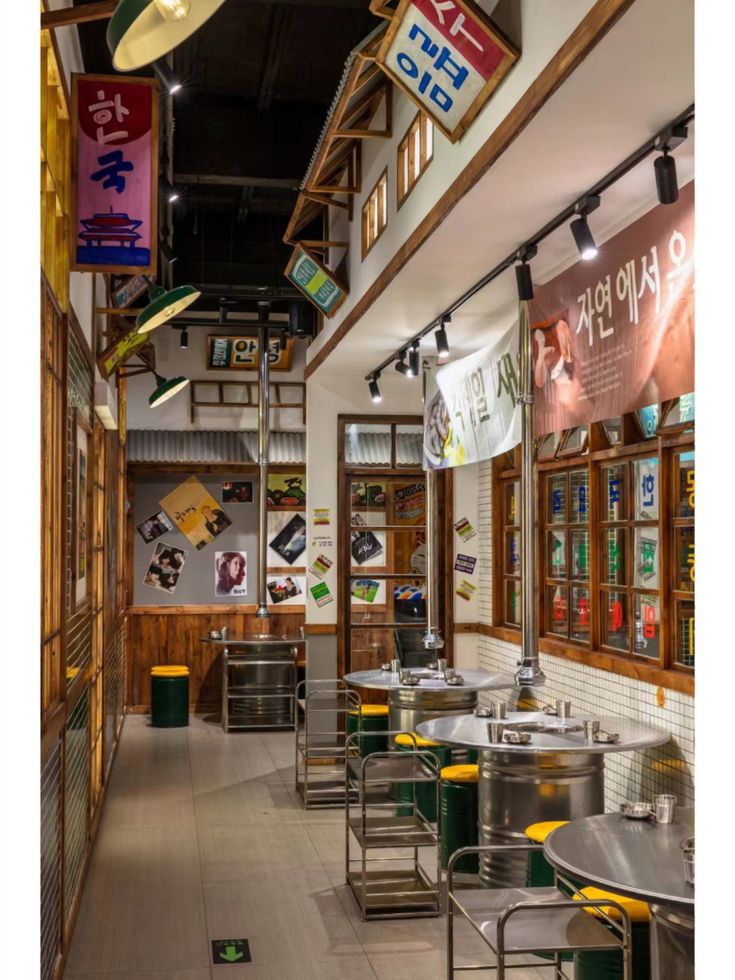 the interior of a restaurant with tables and stools in front of signs hanging from the ceiling