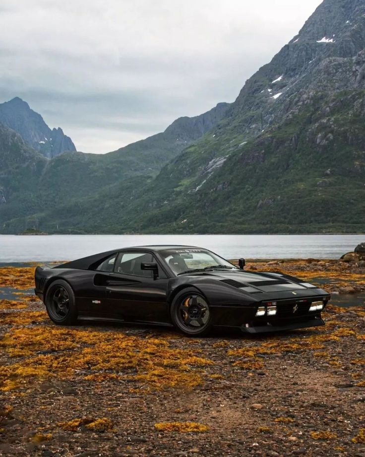 a black sports car parked on the side of a lake with mountains in the background