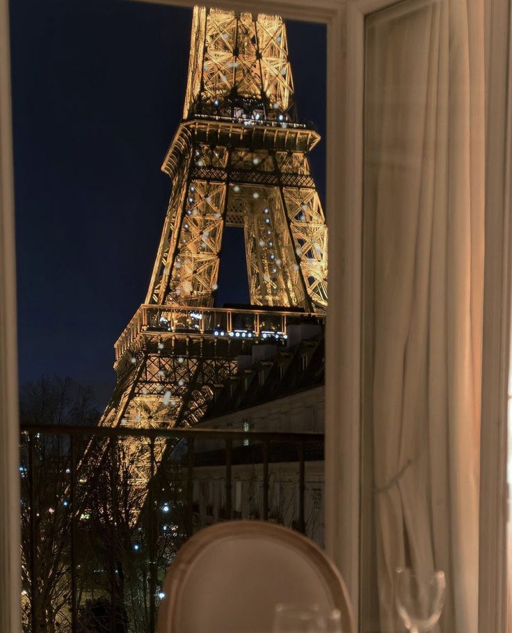 the eiffel tower is lit up at night from inside a hotel room window