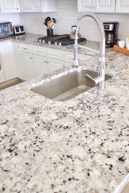 a kitchen with white cabinets and granite counter tops, stainless steel sink and faucet