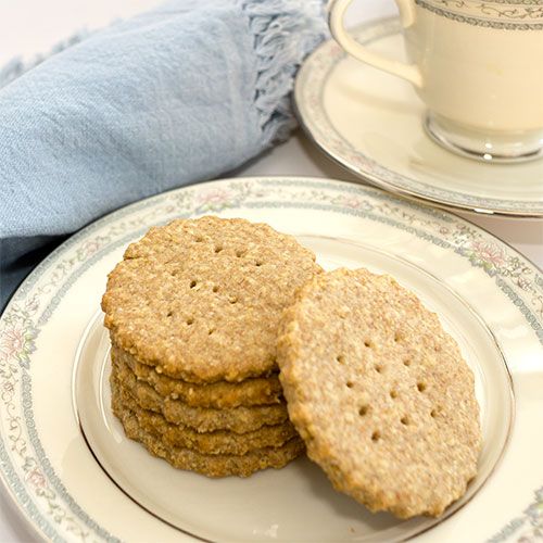 three cookies on a plate next to a cup and saucer with a blue towel