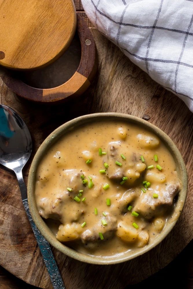 a bowl filled with meat and gravy on top of a wooden cutting board