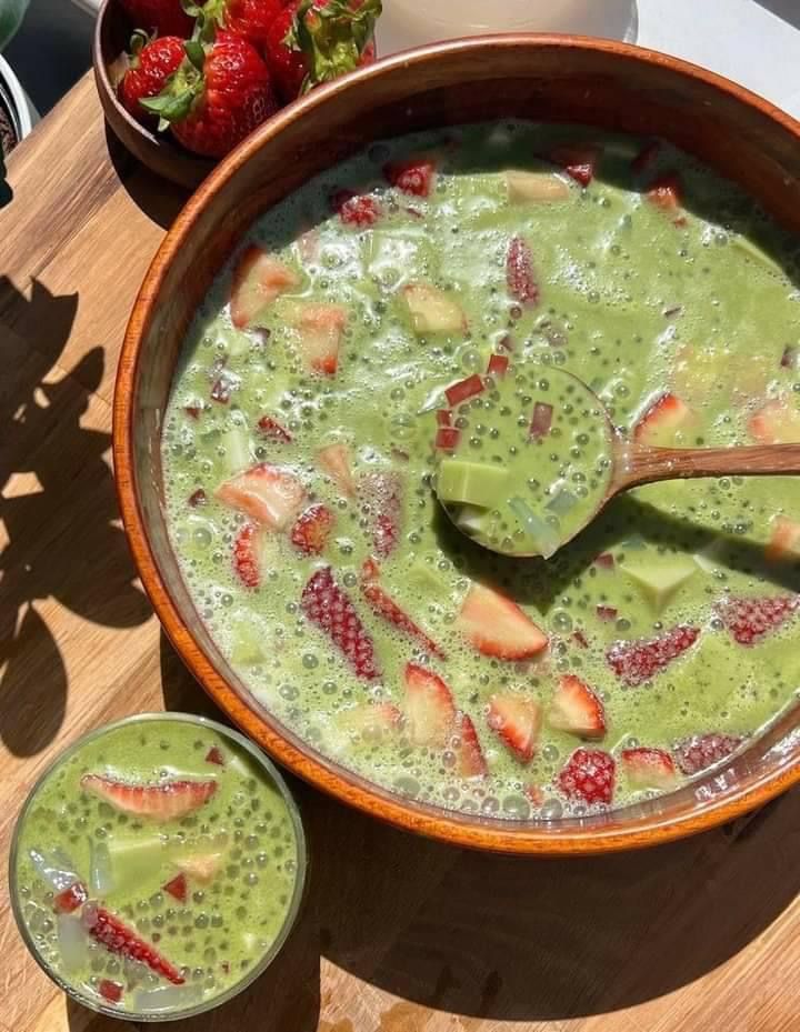 a wooden table topped with a bowl filled with green liquid and strawberries on top of it