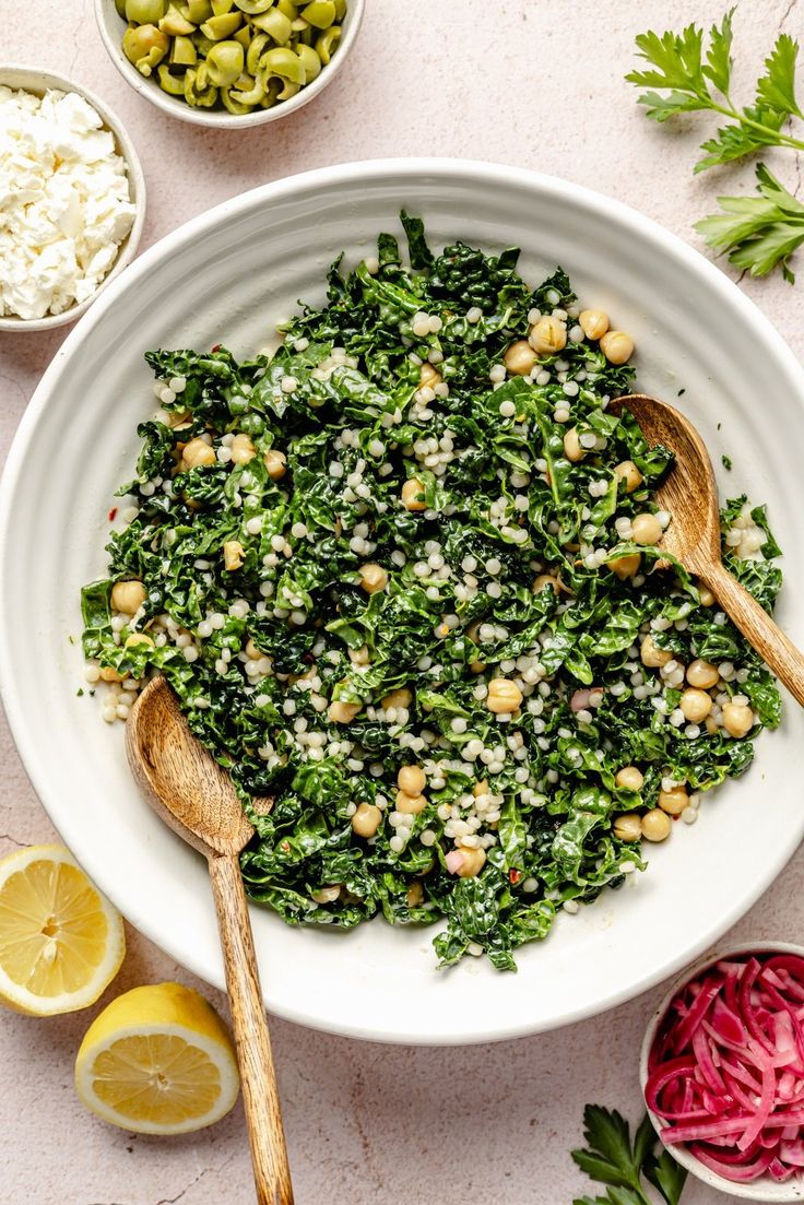 a white bowl filled with greens, beans and feta cheese next to sliced lemons