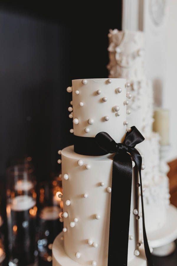 a white and black wedding cake with pearls on the top is adorned with a bow