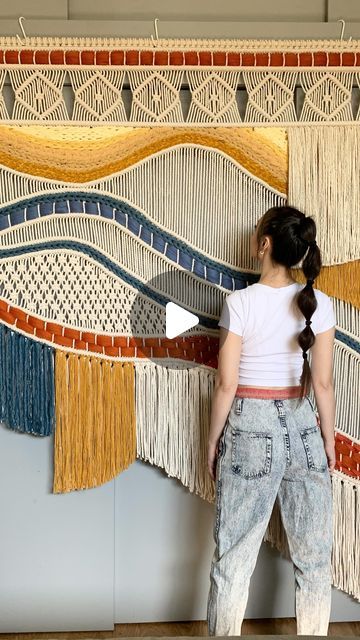 a woman standing in front of a wall hanging with fringes on it's sides