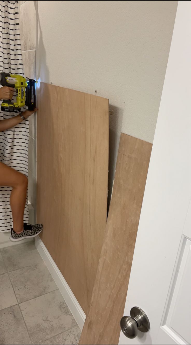 a woman is working on the wall in her bathroom while holding a drill and screwdriver