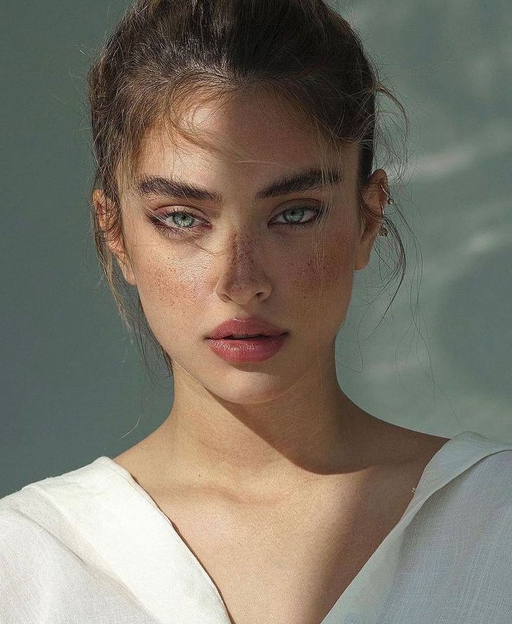 a young woman with freckled hair and blue eyes looks at the camera while wearing a white shirt