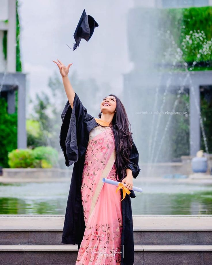 a woman in a graduation gown throwing her cap into the air with a fountain behind her