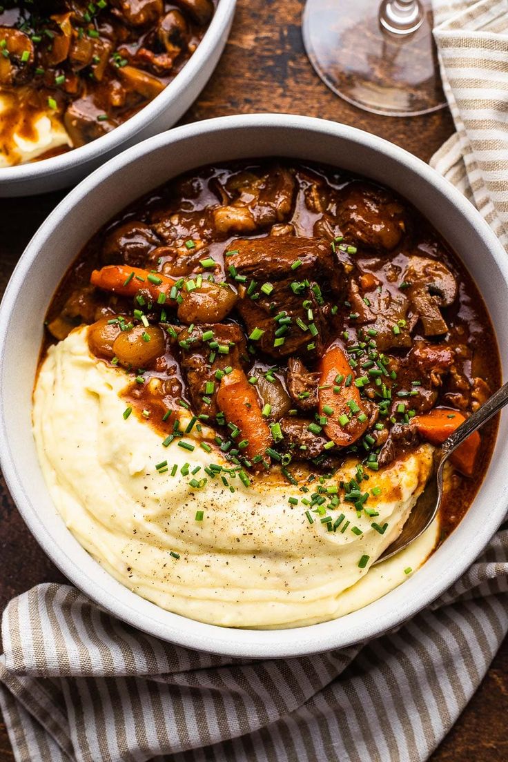 two bowls filled with mashed potatoes and beef stew on top of a wooden table