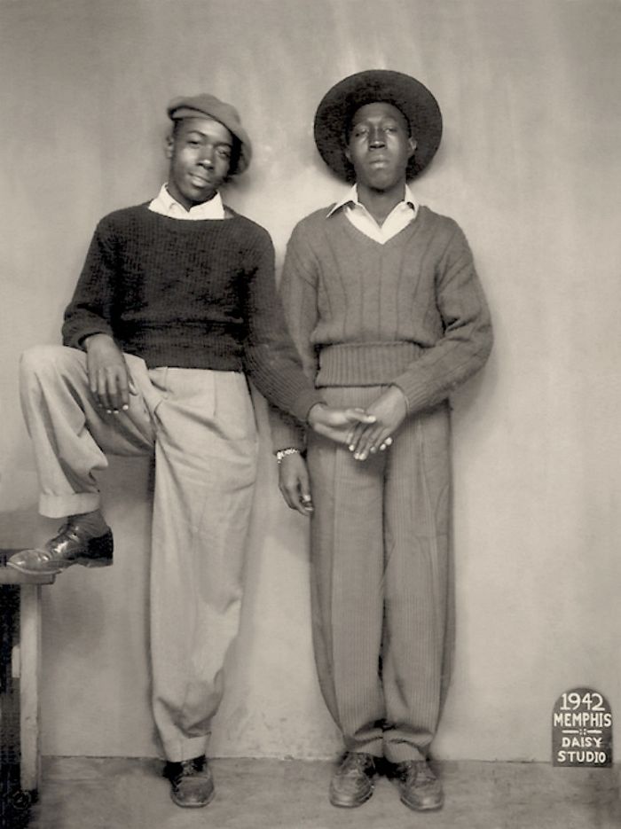 two black men standing next to each other in front of a wall with a clock on it