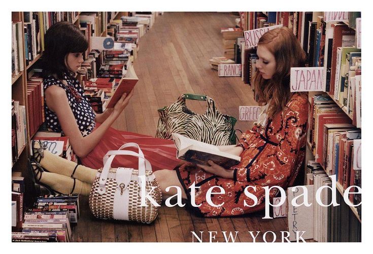 two young women sitting on the floor in front of bookshelves and holding shopping bags