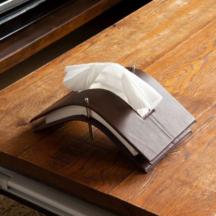 an open book sitting on top of a wooden table next to a white napkin dispenser