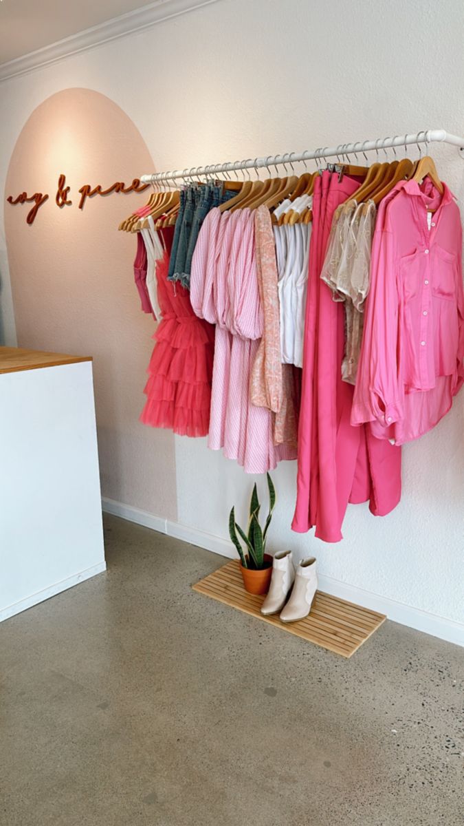 clothes are hanging up in the corner of a clothing store, with shoes on the floor