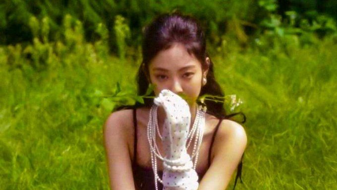 a woman sitting in the grass with her hands on her face and pearls around her neck