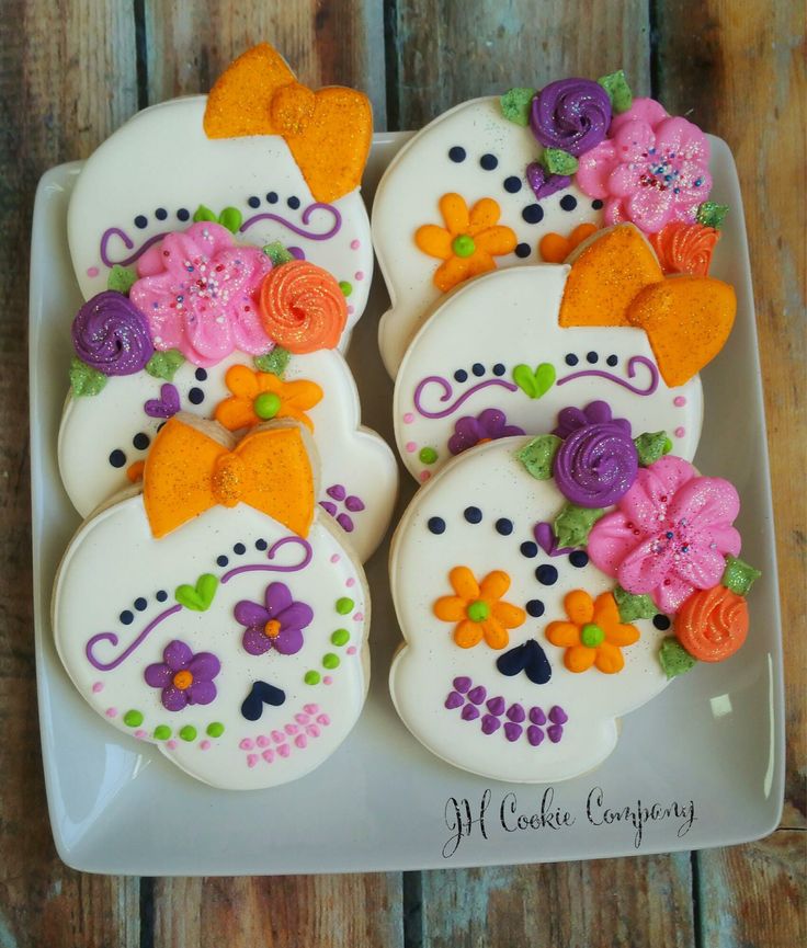 decorated sugar cookies with flowers and skulls on a white plate sitting on a wooden table