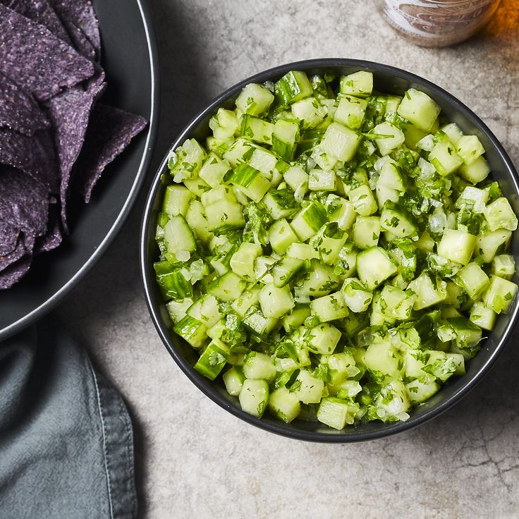 a bowl filled with cucumbers next to a plate of tortilla chips