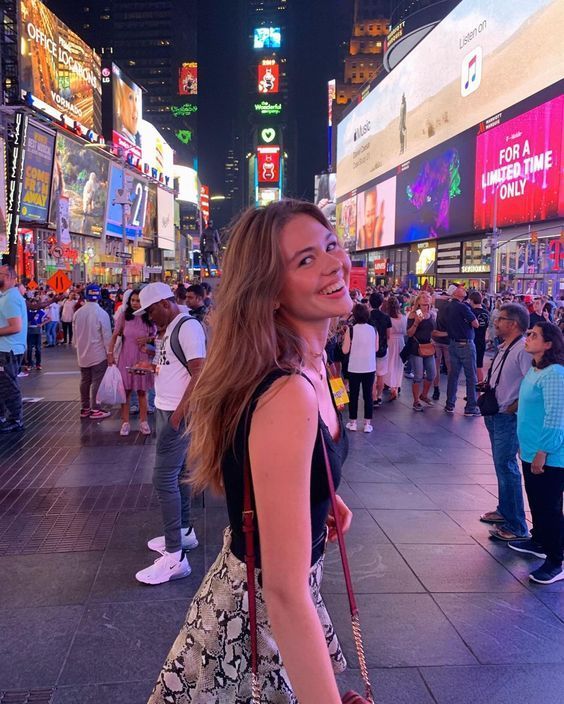 a woman is walking down the street in times square, new york city at night