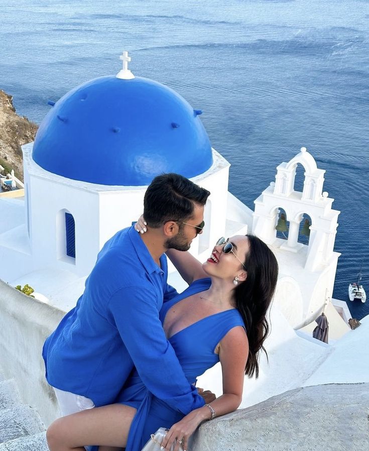 a man and woman leaning on the edge of a wall next to a body of water