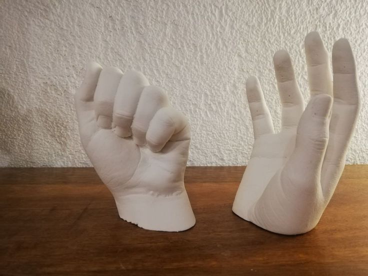 two hands made out of white plastic on a wooden table with a wall in the background