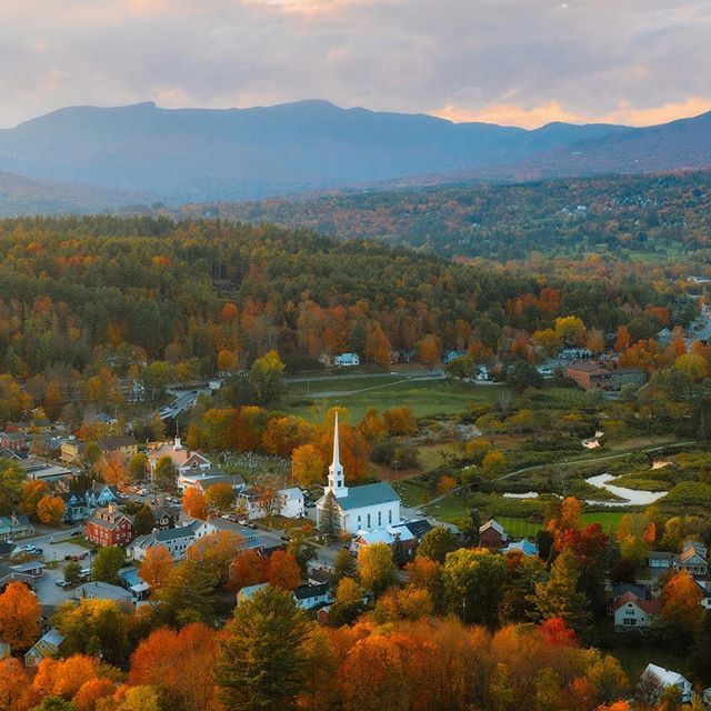 an aerial view of a small town surrounded by mountains and trees in the fall season