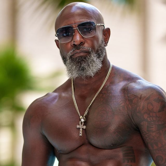 a shirtless man wearing sunglasses and a cross necklace