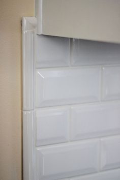 the corner of a kitchen with white tile on the wall and cupboards behind it