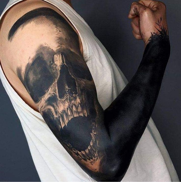 a man with a black and grey skull tattoo on his arm