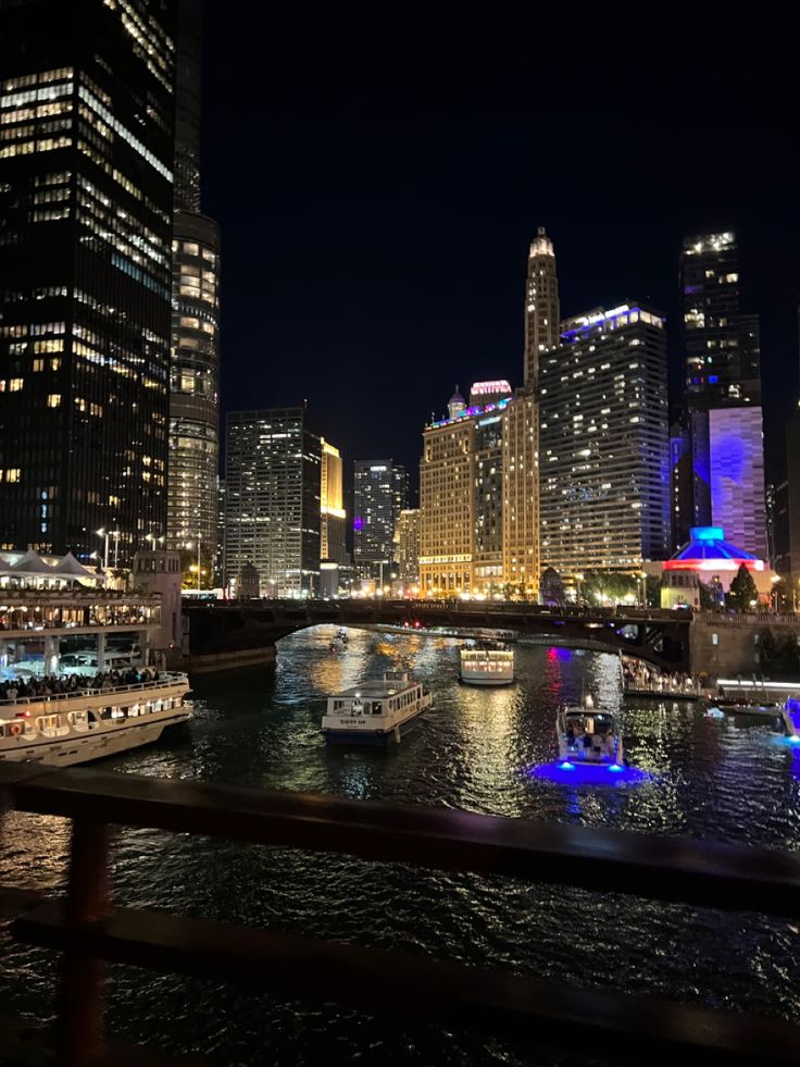 the city skyline is lit up at night with boats in the water and lights on