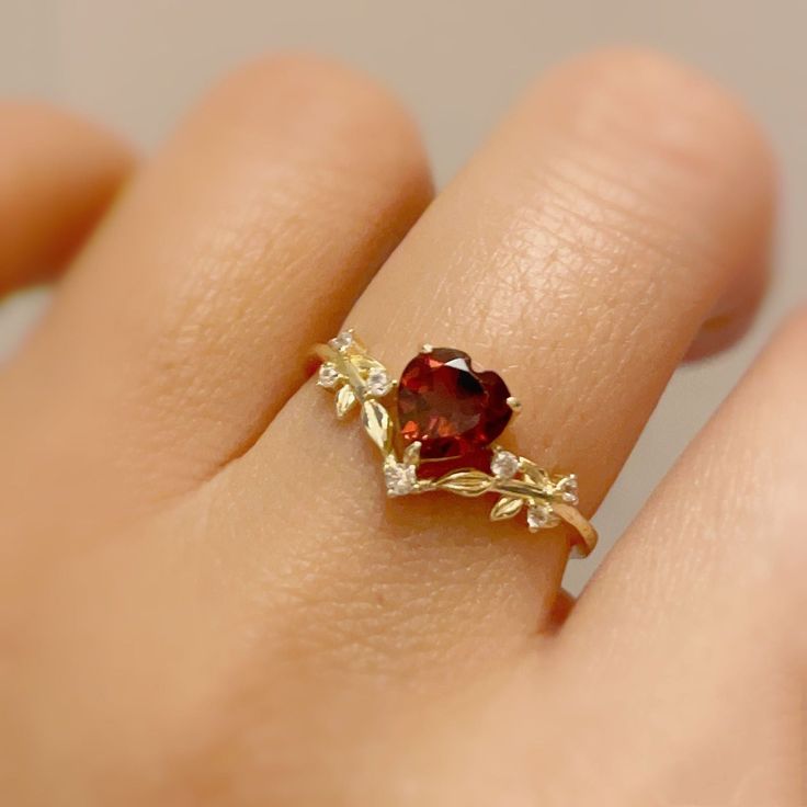 Cue the romance with our stunning Heart’s Desire Red Garnet Ring. This perfect expression of true love features a heart-shaped red garnet center stone along with a curved white topaz leafy band that adds a natural charm. A cherished keepsake that radiates love from every angle. ✦ Available in both 14K yellow gold vermeil (14K yellow gold plated over a sterling silver base) and 10K solid yellow gold. Red Stone Wedding Rings, Heart Shaped Ruby Ring, Garnet Heart Ring, Garnet Promise Rings, Red Rings Engagement, Red Promise Rings, Gold Red Jewelry, Red And Gold Ring, Heart Stone Ring