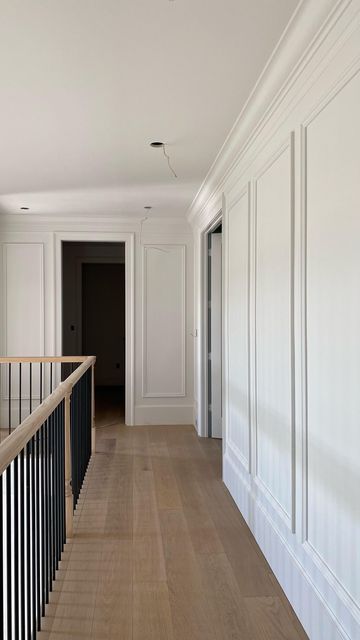 an empty hallway with white walls and wood flooring on the other side, along with black handrails