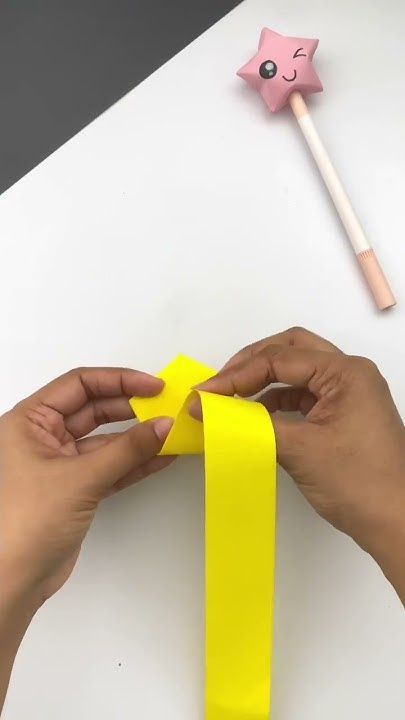 two hands holding a yellow ribbon next to a pink star shaped object on top of a white table