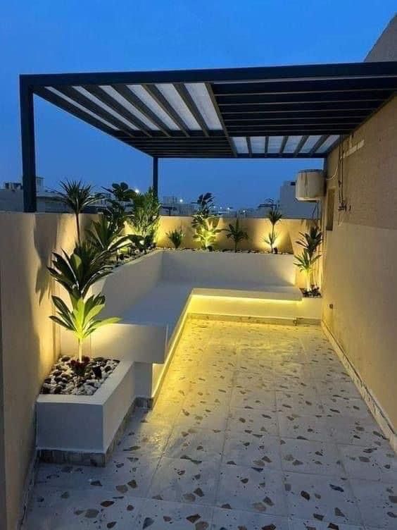 an outdoor area with benches and plants lit up by lights on the side of the building