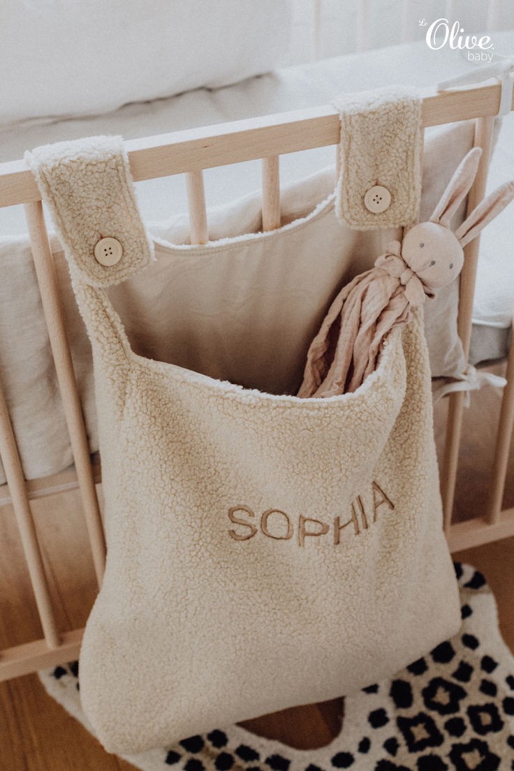 a baby crib with a stuffed animal and personalized name on the front pocket